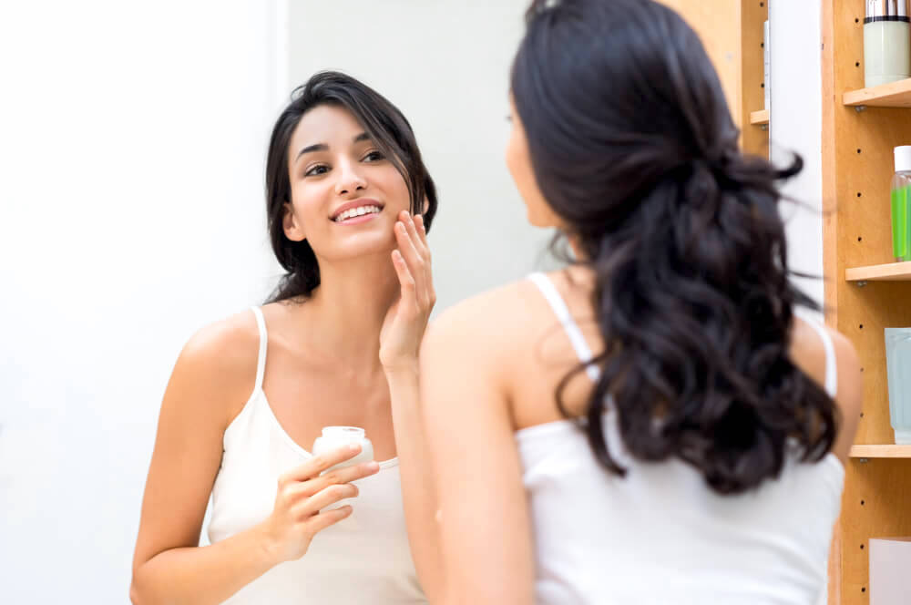 woman applying moisturizer in mirror