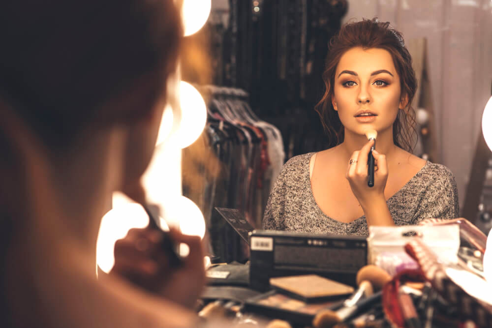 Young woman applying makeup in the mirror