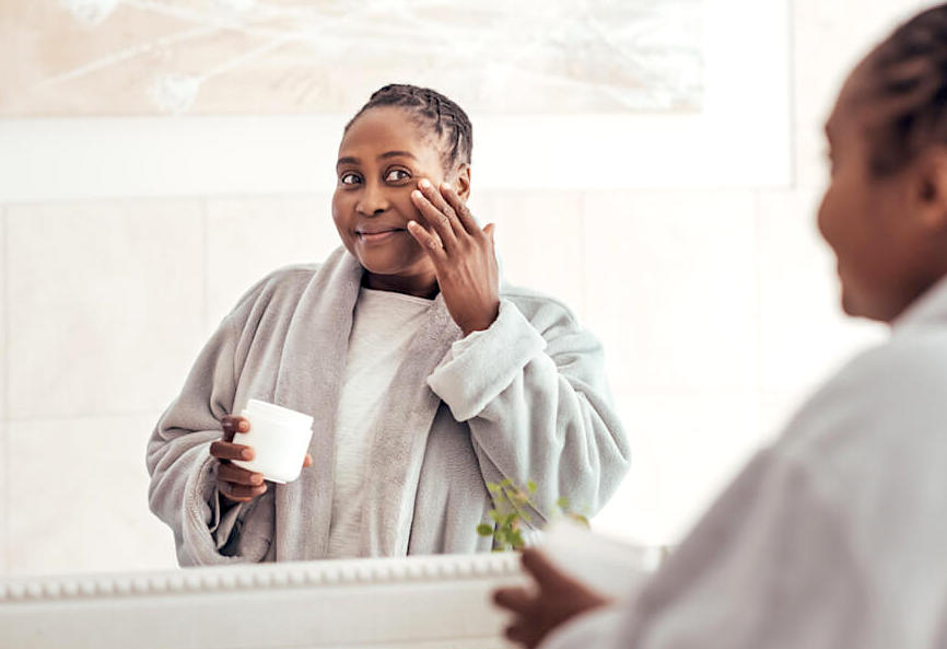 Woman applying face moisturiser in front of bathroom mirror