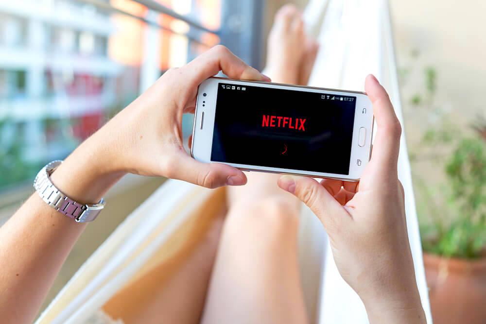 Young woman in a hammock opening Netflix in her smartphone.