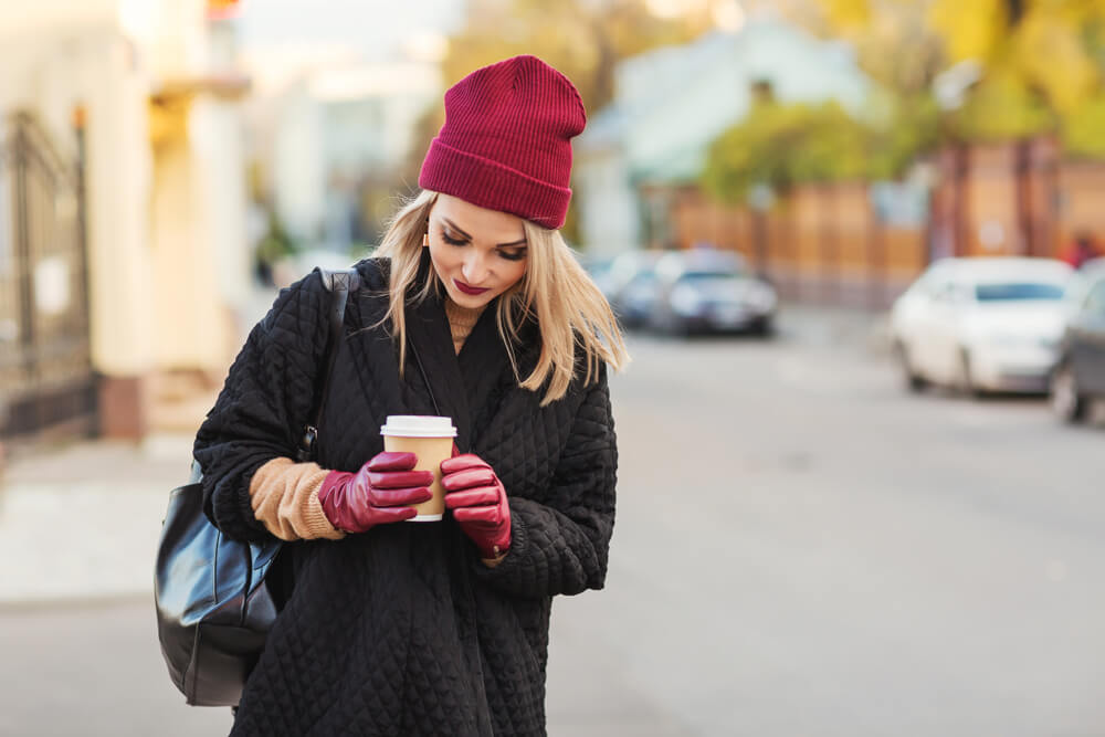 Woman in coat and beanie holding a takeaway cup of coffee