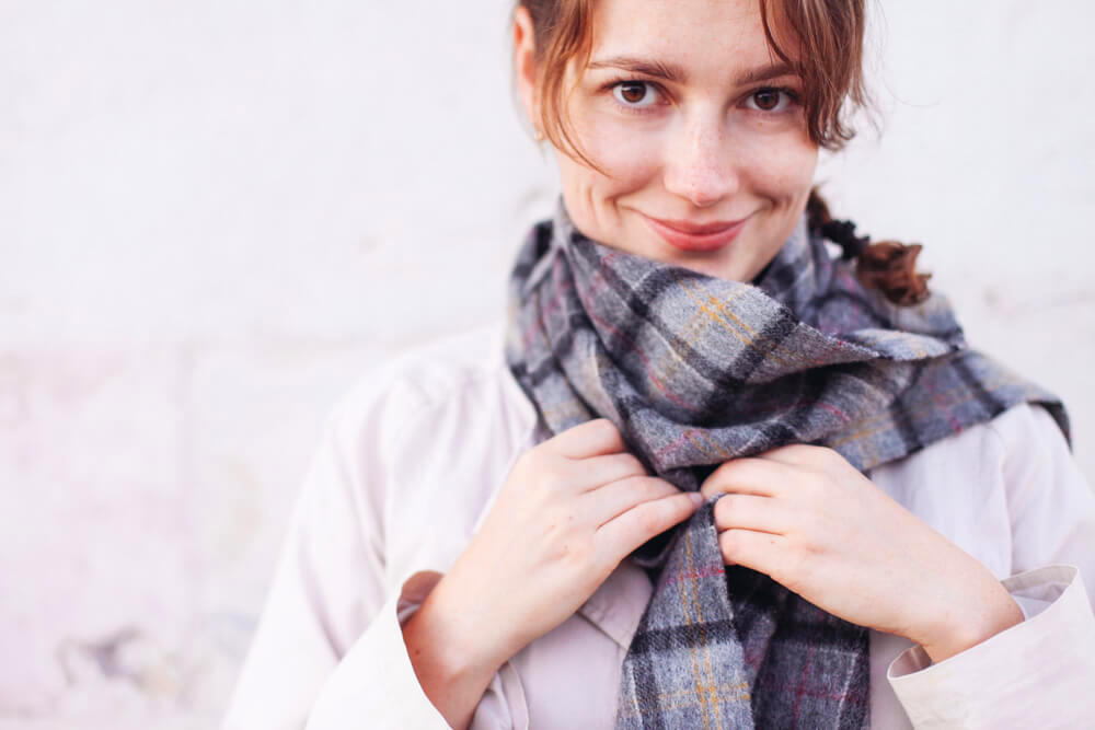 Smiling woman adjusting her grey scarf 