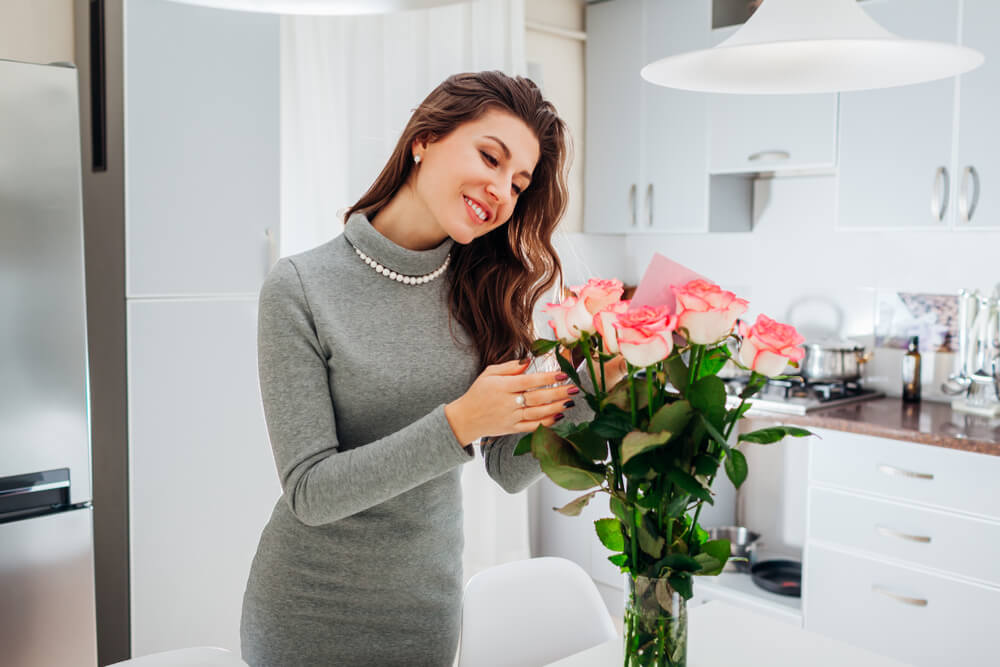Woman arranging fresh flowers in kitchen 