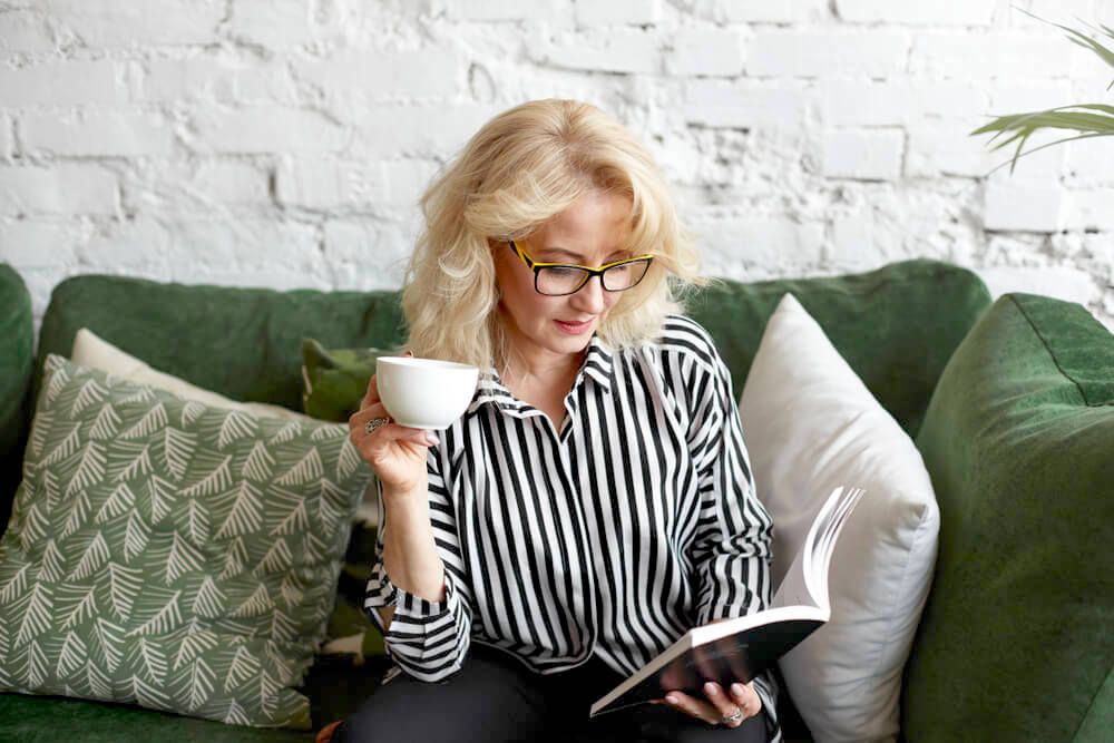 Woman with glasses reading on the couch, holding a cup of coffee