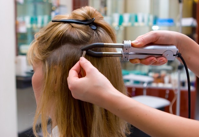 Hairstylist applying hair extensions on client's hair 