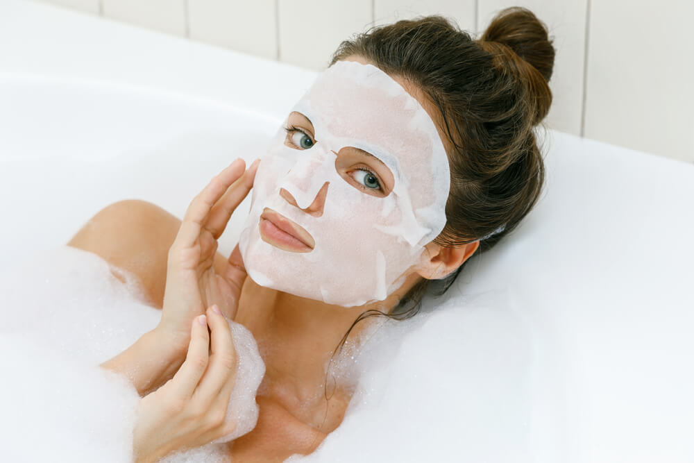Woman with sheet face mask in bath