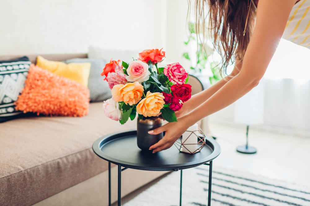 Woman placing vase with flowers on table